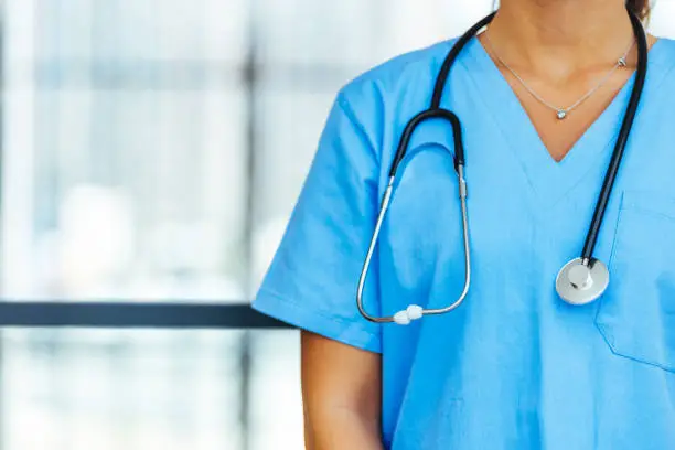 Photo of Unrecognizable female physician in blue medical uniform with stethoscope around neck.