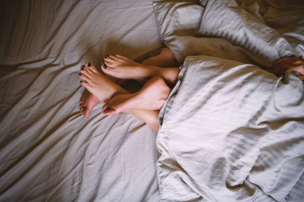 I feel the most beautiful when I fall asleep next to you Lesbian couple lies in bed together, covered with a duvet while their legs are entwined sex and reproduction stock pictures, royalty-free photos & images