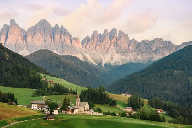 Stunning view of the Funes Valley (Val di Funes) with the Santa Maddalena Church and the mountain range of the Puez Odle Nature Park in the distance during a beautiful sunset. Santa Magdalena, Dolomites, Trentino Alto Adige, Italy.