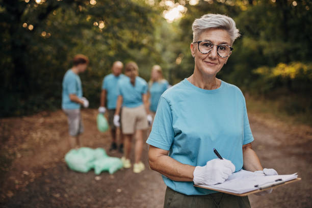 Mature woman volunteer looking at the plans for cleaning garbage in the nature with other volunteers stock photo