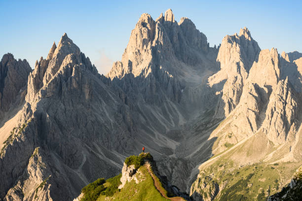 Stunning view of a tourist on the top of a hill enjoying the view of the Cadini di Misurina during sunrise. Cadini di Misurina is a group of mountains located in the Dolomites, Italy. stock photo