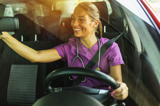 Smiling young nurse driving to work. A female doctor in a uniform with a stethoscope drives her car to work.