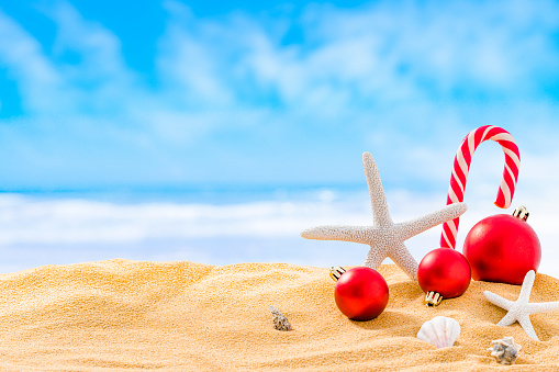 Christmas backgrounds: candy cane, starfish and Christmas ornaments standing on sandy beach with defocused tropical beach at background. High resolution 42Mp outdoors digital capture taken with SONY A7rII and Zeiss Batis 40mm F2.0 CF lens