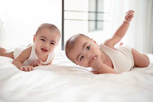 Smiling of newborn twin baby or cute little lying on a white bed at home. Infant child portrait happy concept, Healthy childcare in the morning.