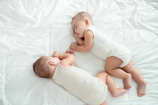 улыбается новорожденный ребенок-близнец или милый малыш, лежащий дома на белой кровати. младенец портрет счастливой концепции, здоровый ух - twin baby newborn baby girls стоковые фото и изображения