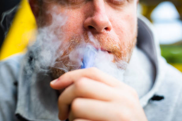 Mid adult male vaping using disposable vape outdoors stock photo