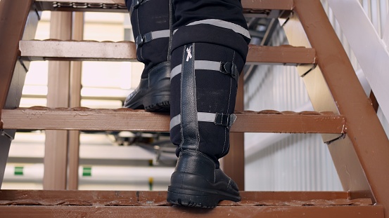 Close-up of a worker descending from a metal ladder in an industrial building in special safety shoes. Work at hazardous facilities, the worker goes down the stairs. Factory worker concept.