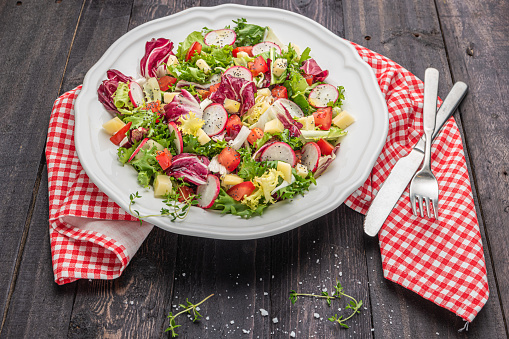 Fresh salad with mixed greens radish cheese and tomato in a plate on wooden background. Italian Mediterranean or Greek cuisine. Vegetarian vegan food. Fresh salad with mixed greens radish cheese and tomato in a plate on wooden background.