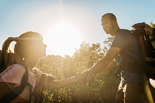 Hiker woman gets help from her boyfriend. A photo of a beautiful and smiling couple helping each other.