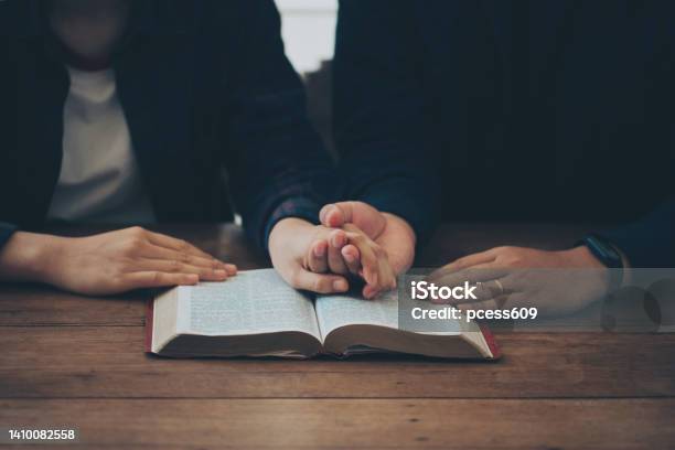 Two Christian Couples Holding Each Others Hands Praying Together Over The Bible On A Wooden Table Begging For Forgiveness And Believing In Goodness Christian Life Crisis Prayer To God Stock Photo - Download Image Now