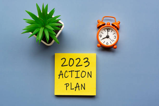 2023 action plan written on Adhesive Note and alarm clock set at 8 o'clock. stock photo