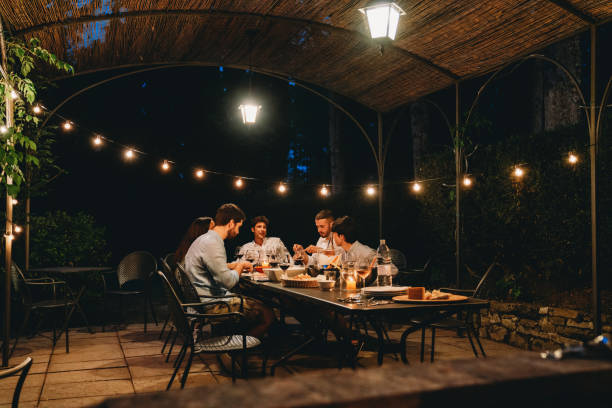 Friends are dining together in a farmhouse at night Friends are dining together in a farmhouse at night. Cozy dinner night in Tuscany, Italy. public lighting stock pictures, royalty-free photos & images