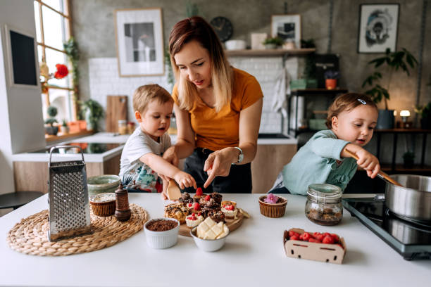 Our cute little mess Mother making cakes in kitchen with her small cute children family dependency mother family with two children stock pictures, royalty-free photos & images