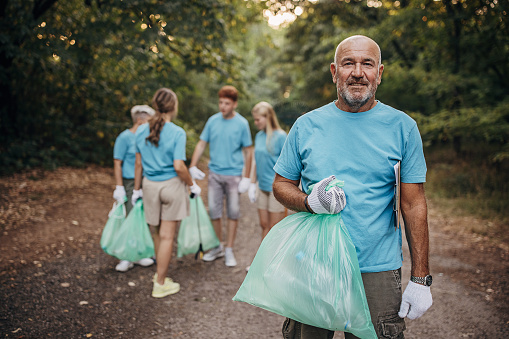 Portrait of senior volunteer while cleaning garbage with group of volunteers in nature