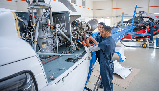 Aero mechanic fixing and checking a helicopter in hangar. Aviation and safety concept.