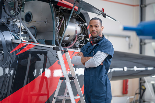 Portrait of male mechanic standing near helicopter in hangar.