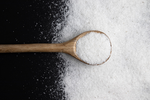 pile of kitchen salt, mineral sea salt in wooden spoon isolated on black background, top view
