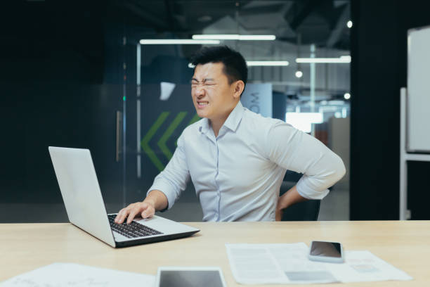 사무실에서 일하는 아시아 사업가, 심한 허리 통증, 노트북으로 일하는 지나치게 피곤한 노동자 - physical injury backache occupation office 뉴스 사진 이미지