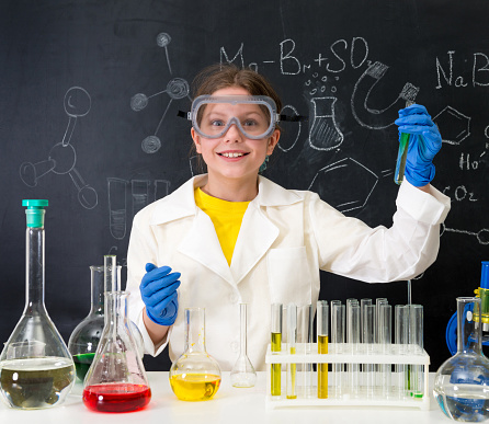 schoolgirl in white gown doing experiments with liquids in chemistry lab