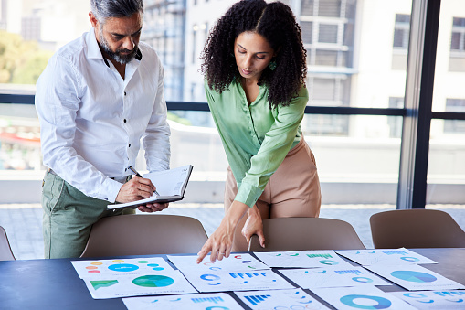 Two diverse businesspeople going over charts and graphs on paper at a conference table in an office boardroom