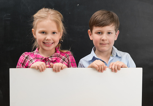 two cute smiling schoolchildren with blank sheet of paper in hands