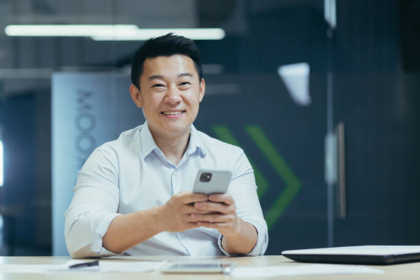 istock Happy Asian man using phone in office, businessman smiling and looking at camera 1410104081