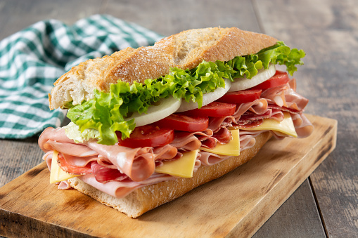 Submarine sandwich with ham, cheese, lettuce, tomatoes,onion, mortadella and sausage on wooden table