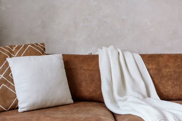 Closeup of eco leather sofa with pillows and white plaid Closeup of brown eco leather couch with soft cushions and knitted white blanket near wall in room indoor. Modern design of living room, dry cleaning furniture concepts leather couch stock pictures, royalty-free photos & images