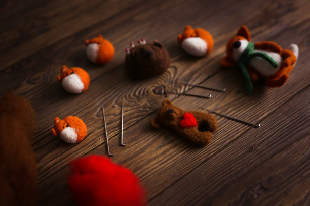toy bear cub with heart made of wool and tools for dry felting, dark brown wooden background,