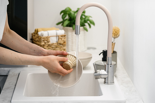 Side view of woman using eco-friendly dishwashing brushes when washing ceramic dishes. Home comfort concept. Eco-friendly kitchenware idea. Cooking at home. Household equipment