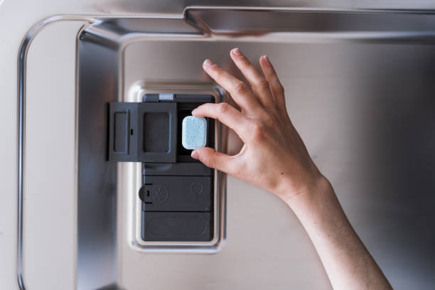 osoba wkładająca kapsułkę do zmywarki, aby rozpocząć czyszczenie płytek - dishwashing detergent zdjęcia i obrazy z banku zdjęć