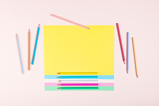 Pencils in pastel colors creatively arranged in a pattern on multicolored papers and a pink background. Back to school concept. Rectangular layout with copy space. Top view, flat lay.