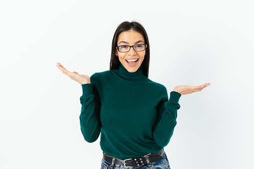 Confident happy young woman wearing glasses, shows gesture spreading her arms to the sides, done, easy, achievement standing on white studio background