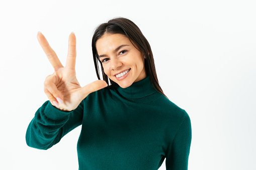 Happy brunette girl, counting three, showing fingers, smiling, standing in white studio