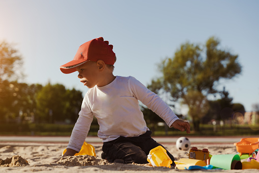 Child sitting in sandbox playing with toy. Little boy having fun on a playground. Summer outdoor activity for kid. Leisure time lifestyle childhood.