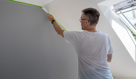 Painter removes masking tape and creates a sharp border between a grey and white painted part of a wall.