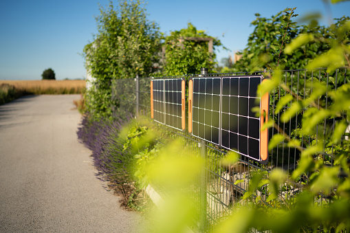Portable solar panels hanging on private garden fence in rural landscape to help owners in times of a possible blackout being a bit self sufficient with using sustainable solar energy