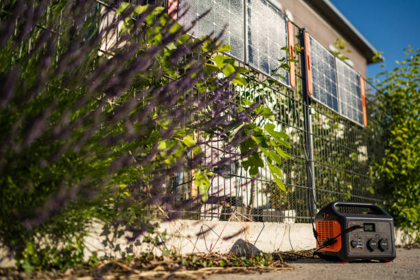 Private black out precaution, battery and portable solar panels producing sustainable energy at garden fence of private house on sunny summer day