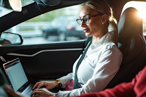 Businesswoman working on laptop while traveling whit man by car