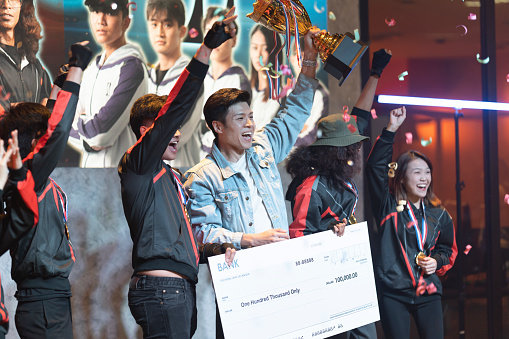 Asian Esports team holding  trophy mock up cheque cheering winning  grand final videogame on stage. Videogame Championship Arena. Cyber Games Tournament Event