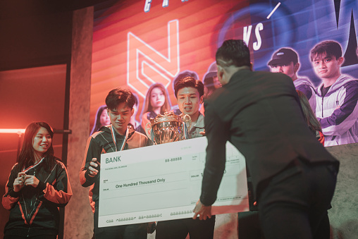 Asian Esports team receiving medals mock up cheque and trophy from emcee celebrating victory cheering winning  grand final videogame on stage. Videogame Championship Arena. Cyber Games Tournament Event