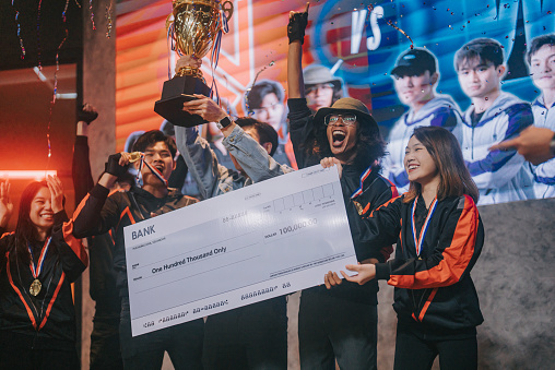 Asian Esports team holding  trophy mock up cheque celebrating victory cheering winning  grand final videogame on stage. Videogame Championship Arena. Cyber Games Tournament Event