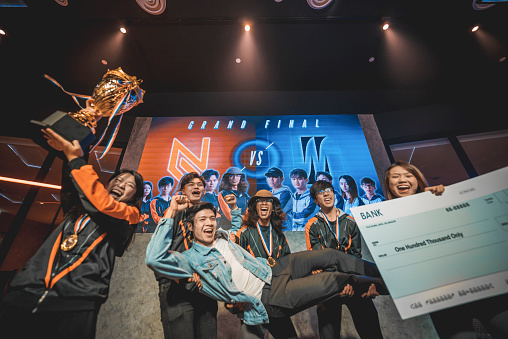 Asian Esports team holding  trophy mock up cheque celebrating victory cheering winning  grand final videogame on stage. Videogame Championship Arena. Cyber Games Tournament Event