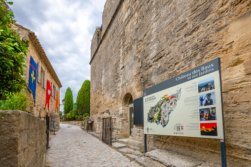A picturesque stone street with a Chateau des Baux castle information sign in the medieval village of Les Baux-de-Provence in the Alpilles mountains of Southern France.