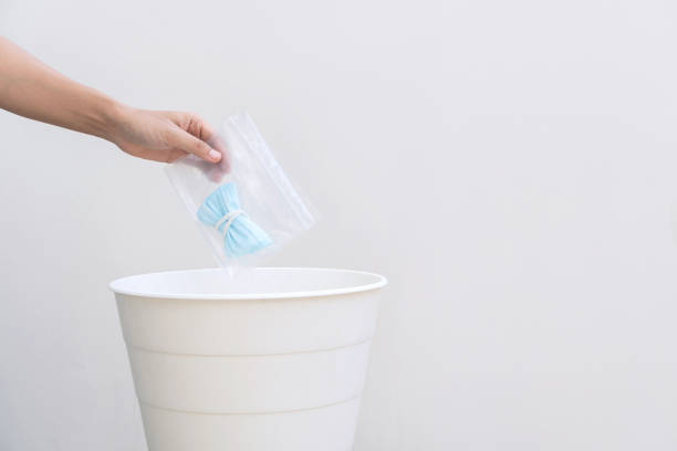 istock Hand drop used protective mask into the trash isolated on white background. Close up, copy space 1410122540