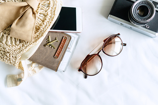 Travel items of a traveler woman with sunglasses, bag, passport and mobile phone on bedroom at home. Travel, journey and holiday concepts. Top view and copy space.