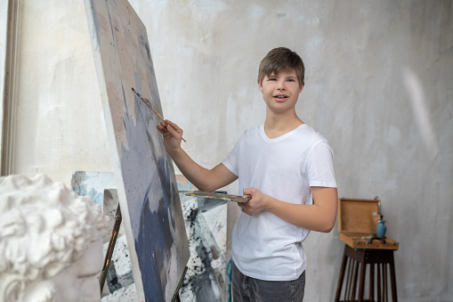 Painting. A boy with down syndrome painting in the studio and looking involved
