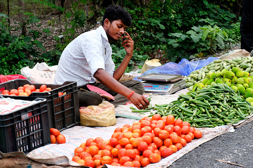 Bagdogra, West Bengal, India. June 24, 2022. A village man sitting on the road side of a busy area in Local Market for sell his vegetables.