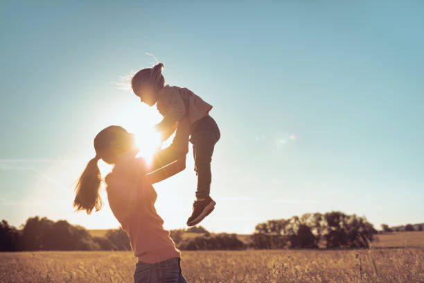Mother holding her daughter up to the sunset sky. stock photo