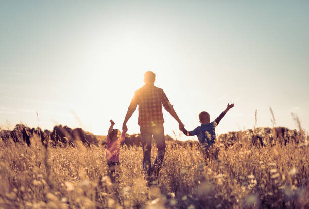 Happy father, children son and daughter walking in a field towards nature sunset stock photo